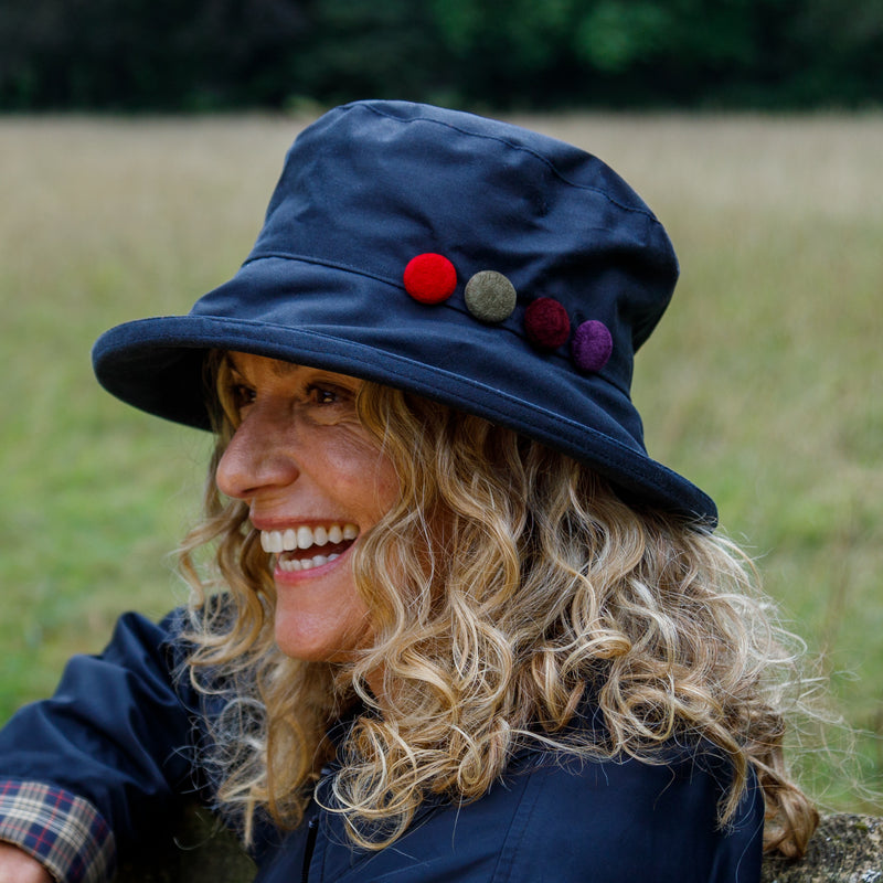 womans peak and brim  navy wax hat with colourful buttons to one side