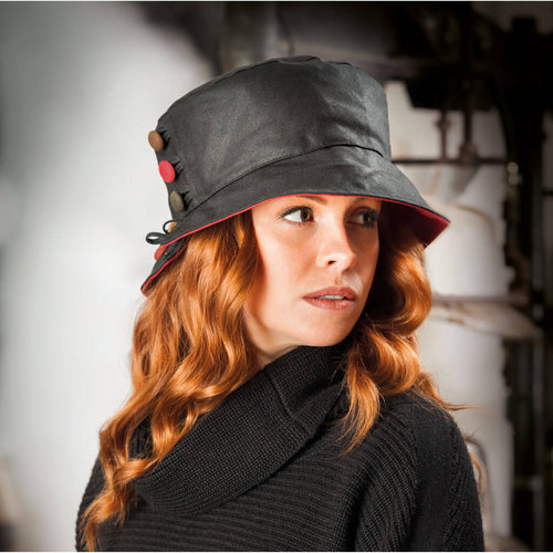 woman wearing black waxed bucket style hat with red underbrim and decorative buttons to one side of hat