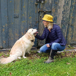 woman wearing yellow rain hat with navy underbrim with dog